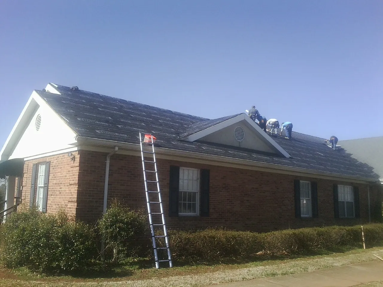Crew tearing shingles off a brick ranch roof with a ladder set — Metal Roof Repair work by our crew in Orient