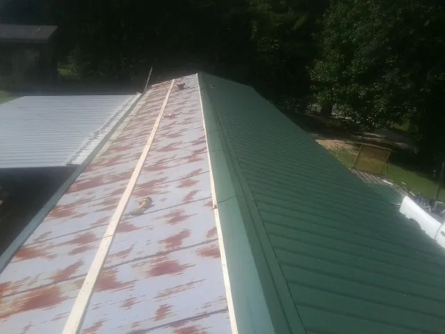 Old rusted panels beside newly installed green metal roofing — Wind Damage Roof Repair by Roofing Brothers in Orient