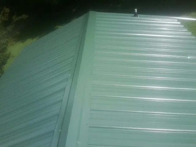 New green metal panels meeting at the ridge of a roof — Flat Roof Repair work by our crew in Orient